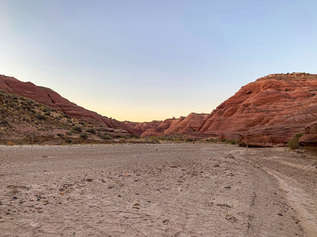 The landscape around a dry upper Paria Canyon glows red with the sunset among rolling sandstone hills