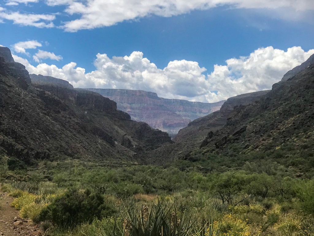 View south on the Arizona Trail down a wide portion of Bright Angel Canyon.  White clouds drift through a blue sky and the South Rim rises in the distanced.