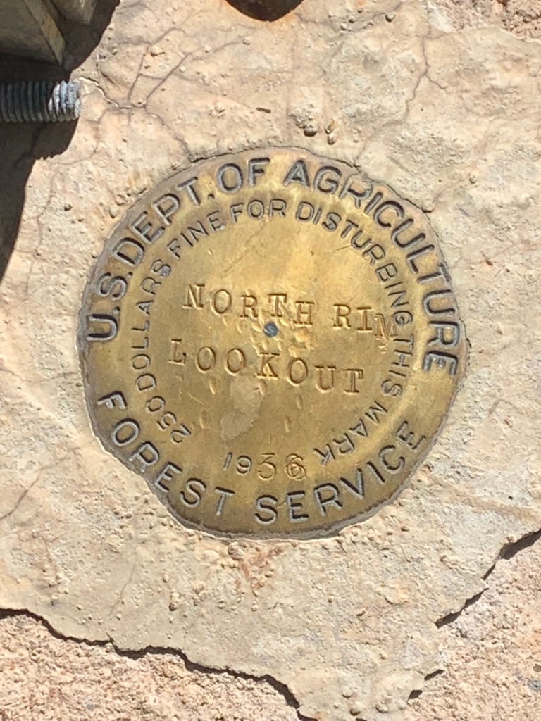 Gold disk engraved "North Rim Lookout" in the center with "US Department of Agriculture" on top and "Forest Service" on the bottom is seen set in concrete at the location of the North Rim Lookout Tower near the Arizona Trail.  This marks the highpoint of the Kaibab Plateau and is near the highpoint of the Arizona Trail.  
