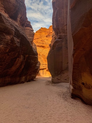Shade and light create alternate dark and bright orange walls under a blue and white sky in Buckskin Gulch, the longest and deepest slot canyon in the world, as it heads upstream toward its junction with Wire Pass.