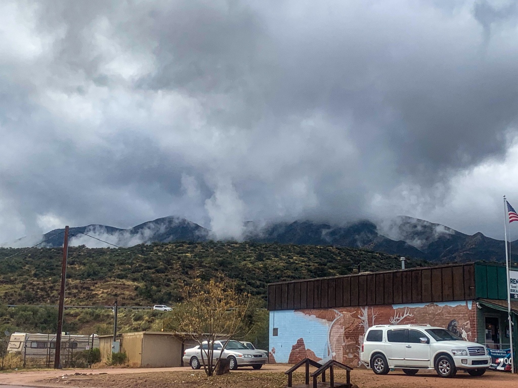 Dark grey clouds drift over the mountains above the town of Tonto Basin below, obscuring the view of the prominent Four Peaks.